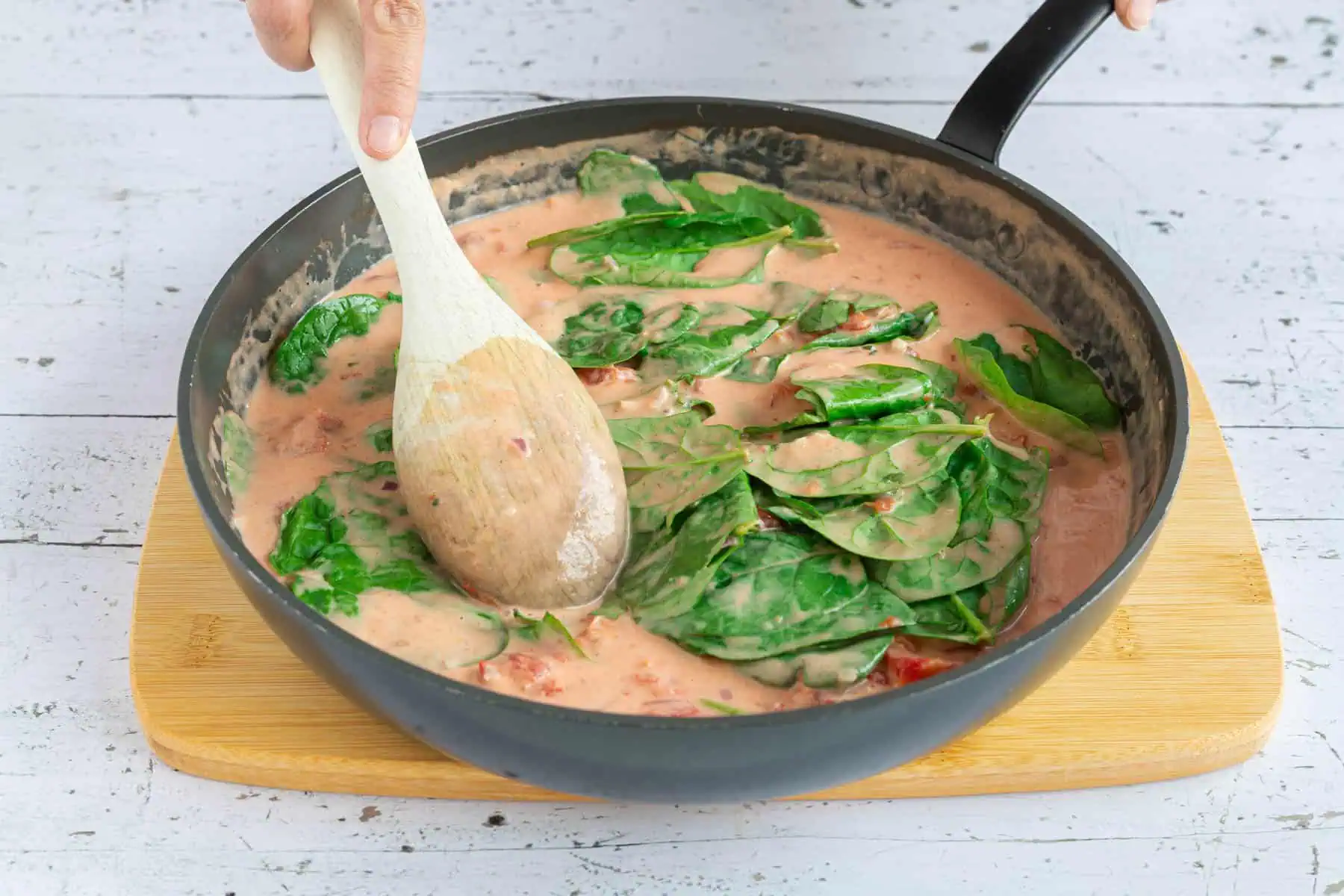 Tomaten-Sahne-Sauce mit Spinat wird für Tortellini-Auflauf in einer Pfanne zubereitet.