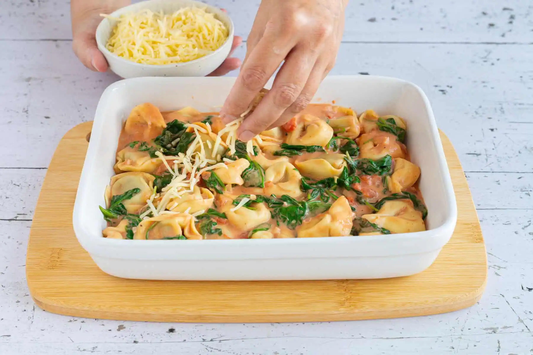 Tortellini mit Spinat-Sauce geschichtet in einer Auflaufform wird mit Käse bestreut.